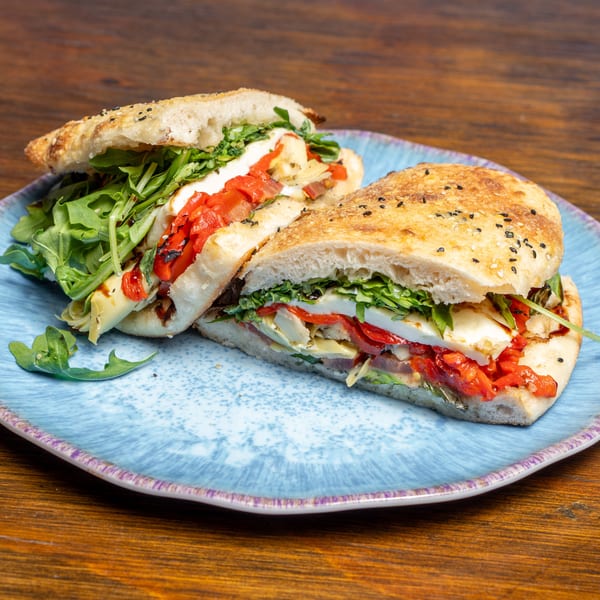 Two halves of a focaccia sandwich filled with arugula, roasted red peppers, and cheese on a blue plate.