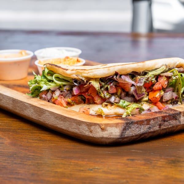 A pita bread sandwich filled with lettuce, tomatoes, and onions, served with two dipping sauces.