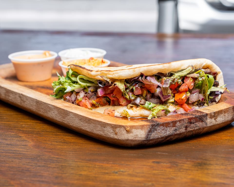 A pita bread sandwich filled with lettuce, tomatoes, and onions, served with two dipping sauces.
