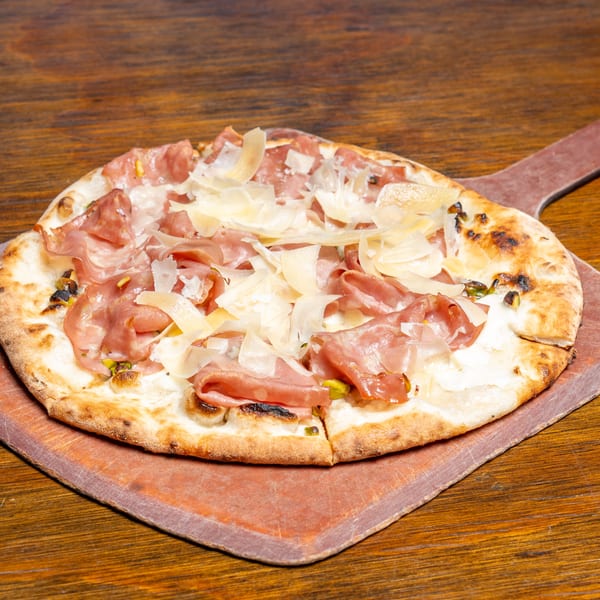 A prosciutto and parmesan pizza on a wooden pizza peel, resting on a dark wooden table.
