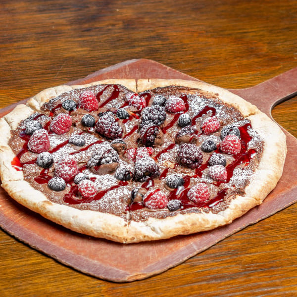 Dessert pizza with chocolate spread, raspberries, blueberries, blackberries, powdered sugar, and berry drizzle.