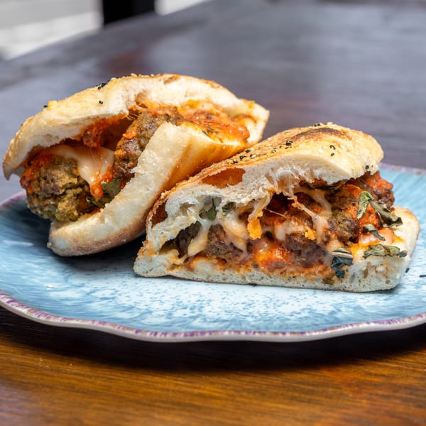 Two halves of a meatball sub sandwich with melted cheese and sauce on a blue plate.