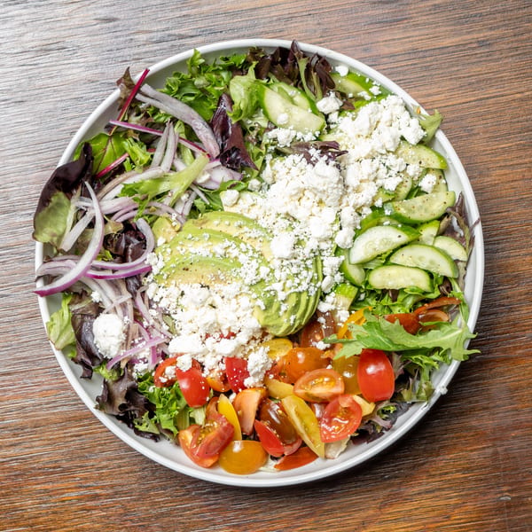 A vibrant salad with mixed greens, red onions, avocado, cucumbers, cherry tomatoes, and feta cheese.