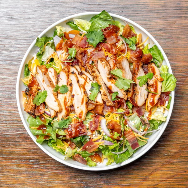 Overhead view of a BBQ chicken salad with bacon, cheese, red onion, and cilantro.