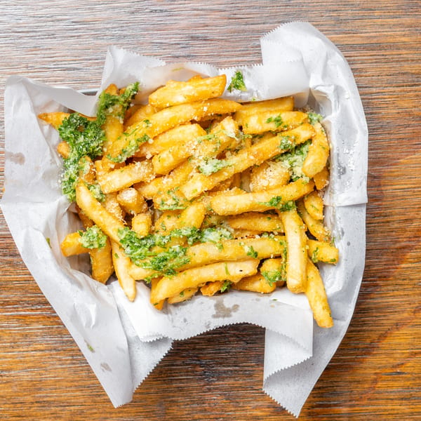 Golden french fries topped with green herbs and grated cheese, served in a paper-lined basket.