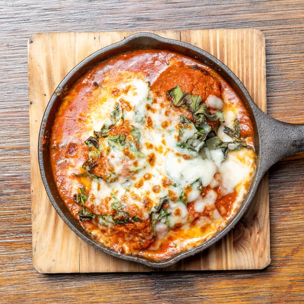 Baked pasta with melted cheese, tomato sauce, and basil in a cast iron skillet on a wooden board.