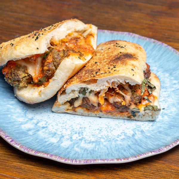 Two halves of a meatball sub sandwich with melted cheese and sauce on a blue plate.