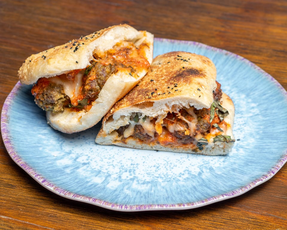 Two halves of a meatball sub sandwich with melted cheese and sauce on a blue plate.